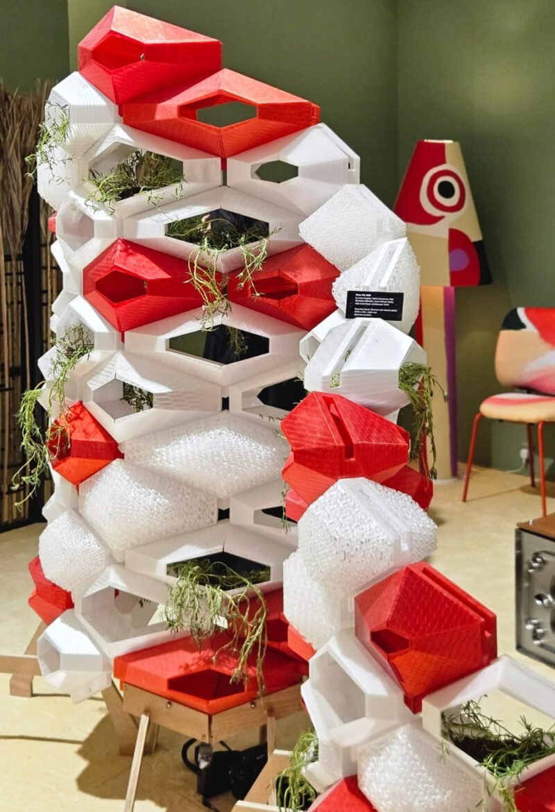 Uma divisória modular que une impressão 3D e biofilia. A estrutura geométrica, em vermelho e branco, funciona como uma colmeia high-tech, integrando plantas ao design. Uma solução funcional e escultural para dividir espaços.