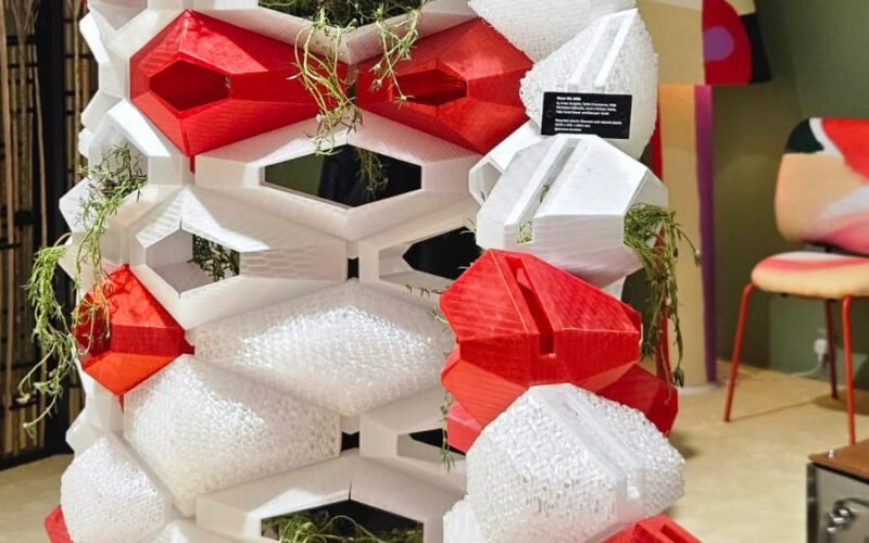 Uma divisória modular que une impressão 3D e biofilia. A estrutura geométrica, em vermelho e branco, funciona como uma colmeia high-tech, integrando plantas ao design. Uma solução funcional e escultural para dividir espaços.
