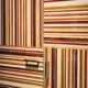 Marcenaria como obra de arte. Este armário usa lâminas de madeira em tons quentes (vermelho, amarelo, marrom) para criar um padrão gráfico de listras. A alternância entre horizontal e vertical, combinada com puxadores modernos, resulta em um design arrojado e luxuoso.