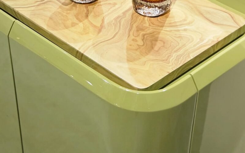 Design que une cor e textura. O aparador destaca-se pelas curvas suaves e pela laca brilhante em tom verde-oliva. O tampo rebaixado em madeira natural aquece a peça, enquanto os vidros âmbar texturizados adicionam um ponto de luz sofisticado.