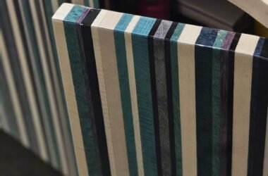 A marcenaria como arte. Este móvel revela sua sofisticação nas bordas e na porta curva, feitas de madeira laminada (multilaminado). As listras em tons de azul, verde, preto e natural criam um padrão gráfico vibrante. Um design que celebra o material.