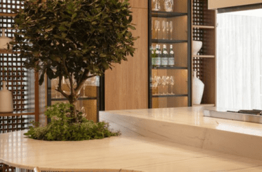 Cozinha americana com balcão integrado, marcenaria em tons de bege e azul, bancada branca e cadeiras de madeira. Exemplo de ergonomia de cozinha para apartamentos modernos.