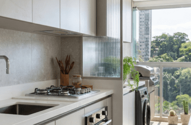 Cozinha planejada clean integrada à área de serviço com divisória de vidro canelado em estrutura cinza. Detalhe de lavanderia escondida no armário de forma parcial em apartamento moderno.