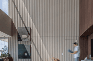 Detalhe de sala alta com estante de madeira do chão ao teto e quadros para paredes altas estrategicamente posicionados para valorizar a verticalidade.