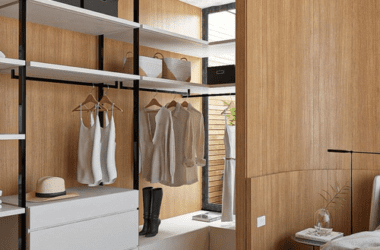 Closet aberto planejado em madeira escura com nichos iluminados por fitas de LED verticais e roupas organizadas por cores. Exemplo de vantagens closet aberto.