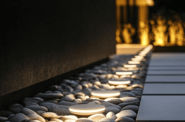 Fachada de casa de luxo à noite com iluminação de destaque em colunas, jardins e reflexos nos grandes vãos de vidro.